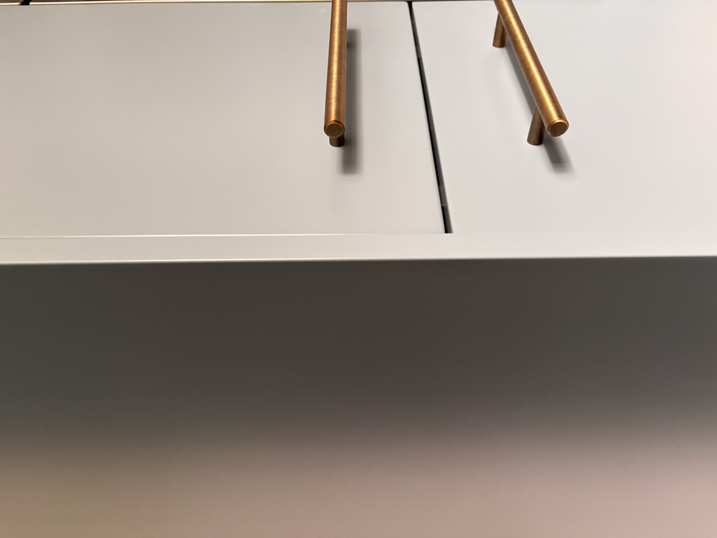 Close-up of a white cabinet with gold-colored handles and a black line running between the doors.