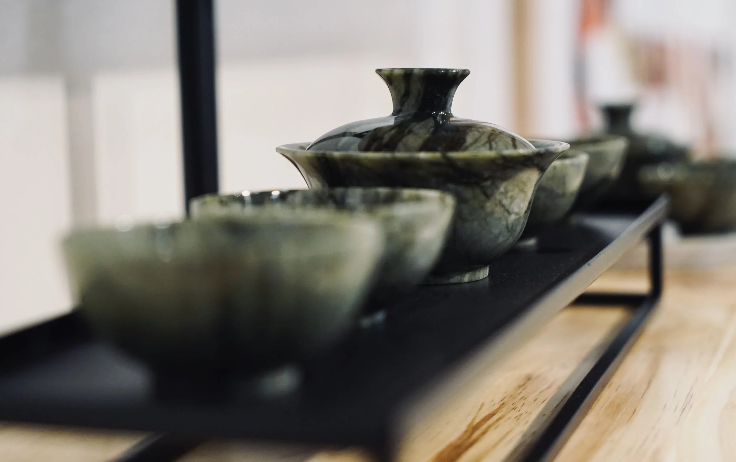 A set of green and black marbled ceramic bowls and vases displayed on a black rack on a wooden surface.