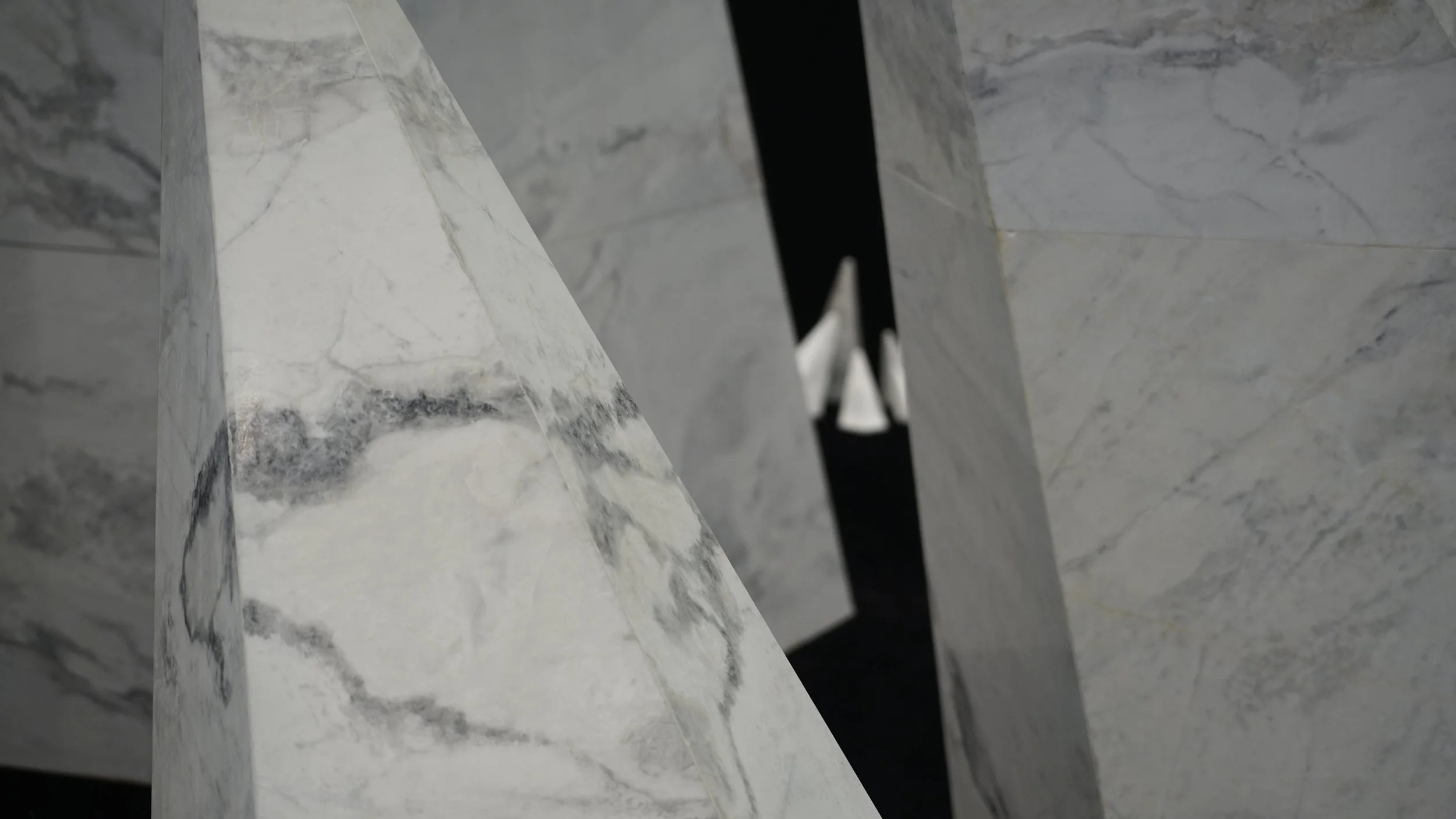 Close-up of a marble sculpture with angular shapes and black background, showcasing white and grey veined marble surfaces.