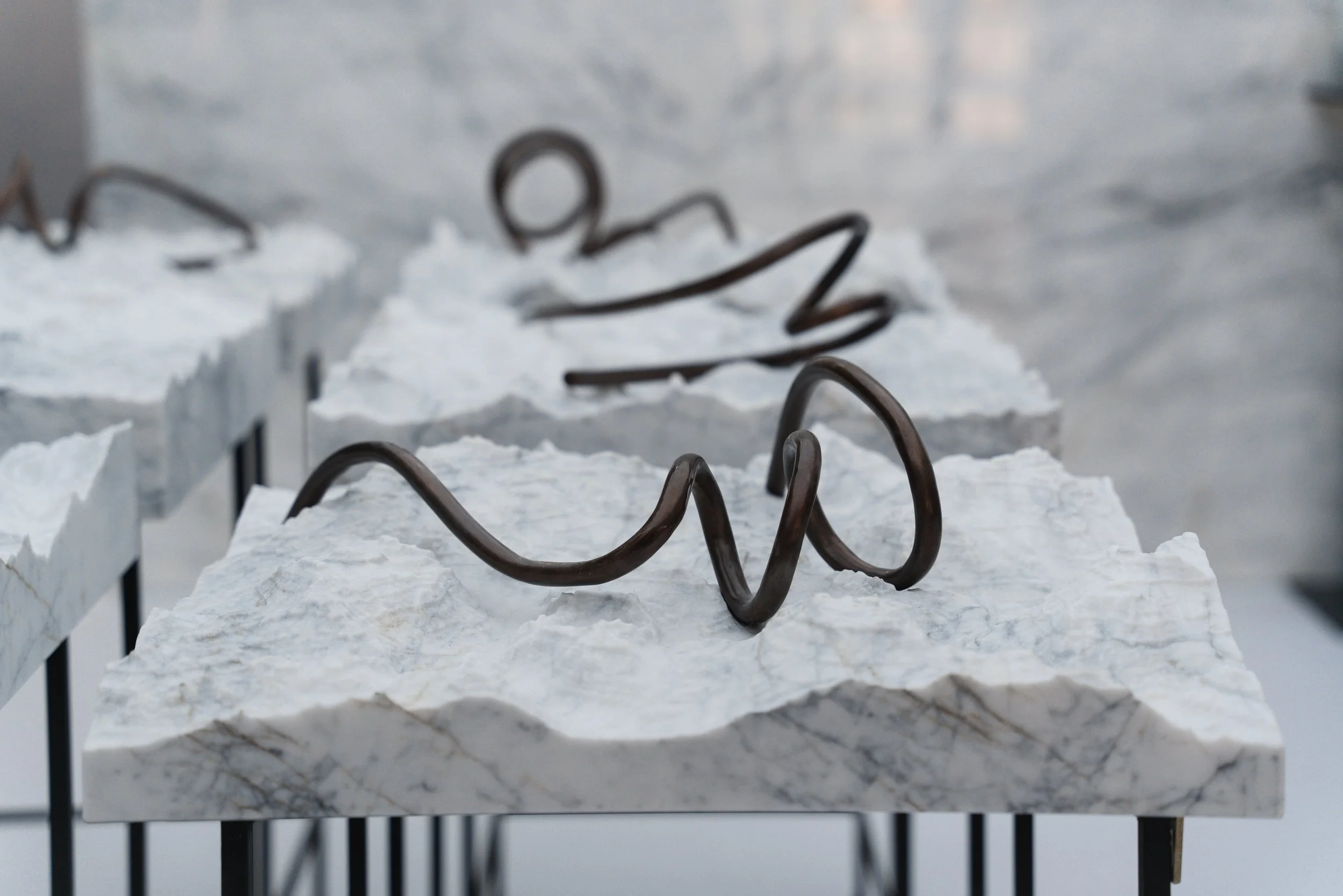 Close-up of a twisted metal sculpture on rough white marble slabs with a blurred background.