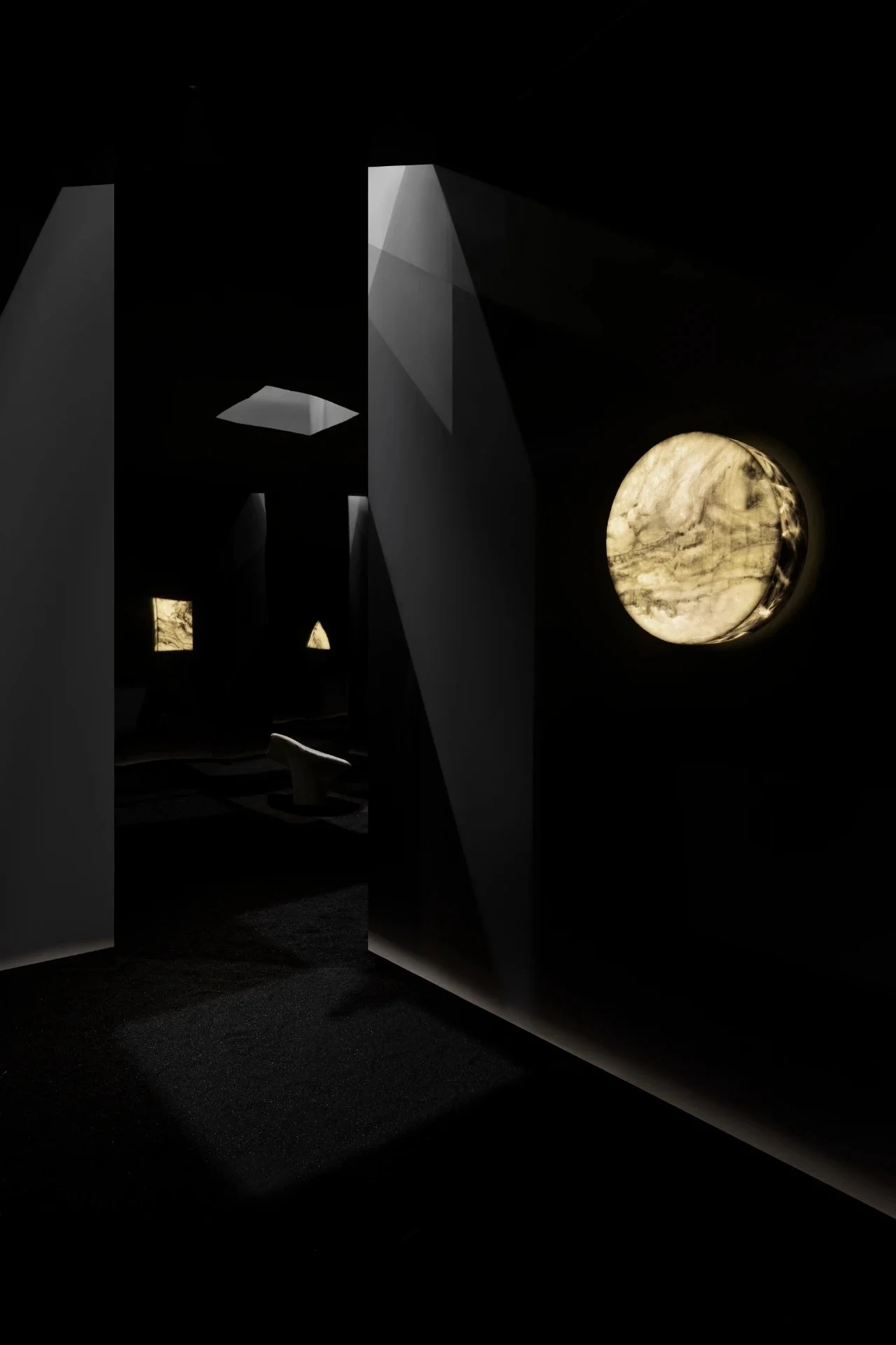 Interior museum exhibit with black walls and illuminated moon-like sculpture