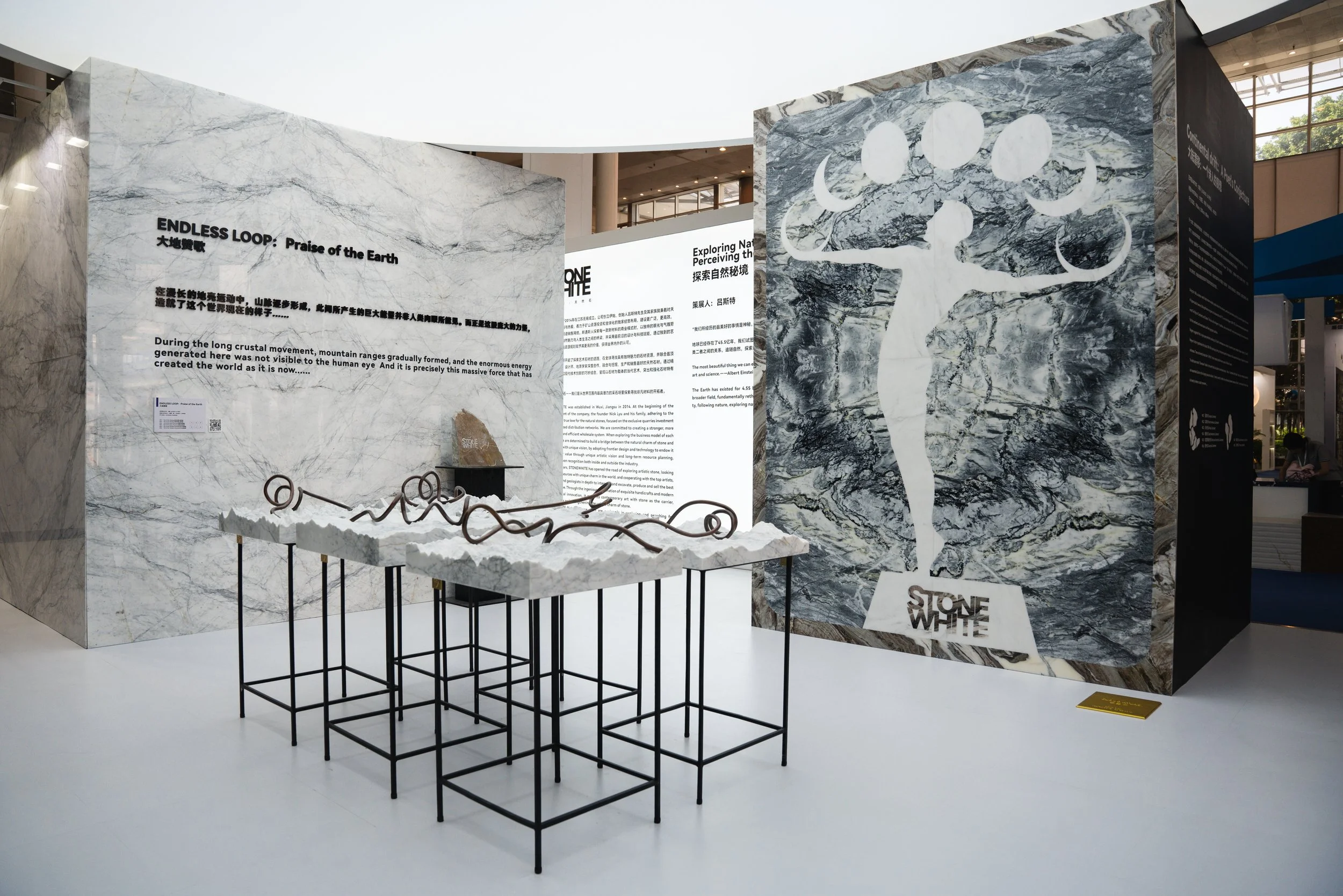 Exhibition display with marble panels, stone sculpture, and metal art piece about Earth's geological features and movement.