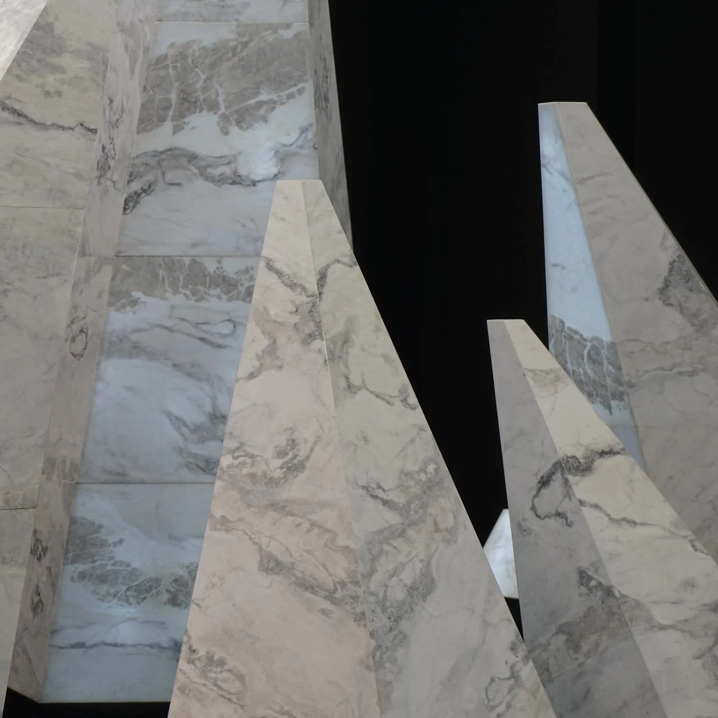 Close-up view of large marble sculptures with pointed shapes and gray and white veining, set against a dark background.