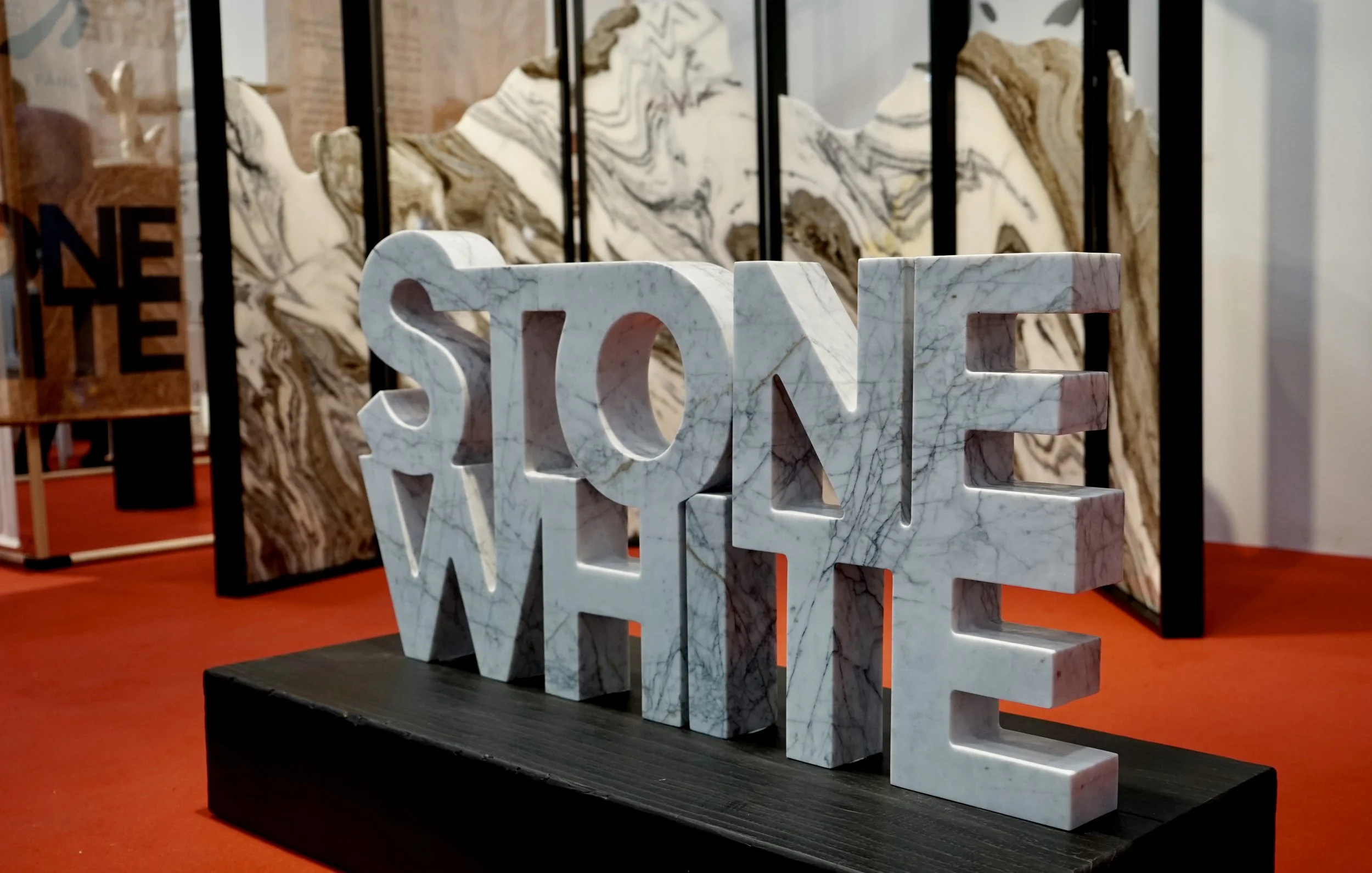 Marble sculpture spelling out the word "LOVE" on a black base, with sculpted marble slabs behind it in a store or gallery setting.