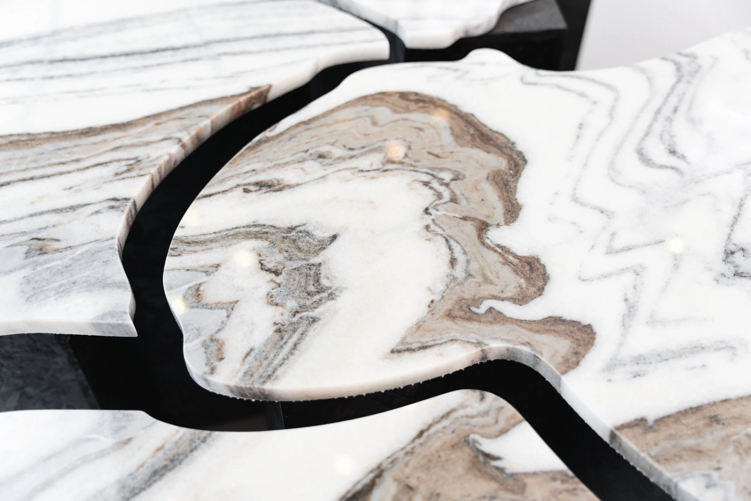 Close-up view of a marble table with a black inlay, featuring white, beige, and gray swirling patterns.