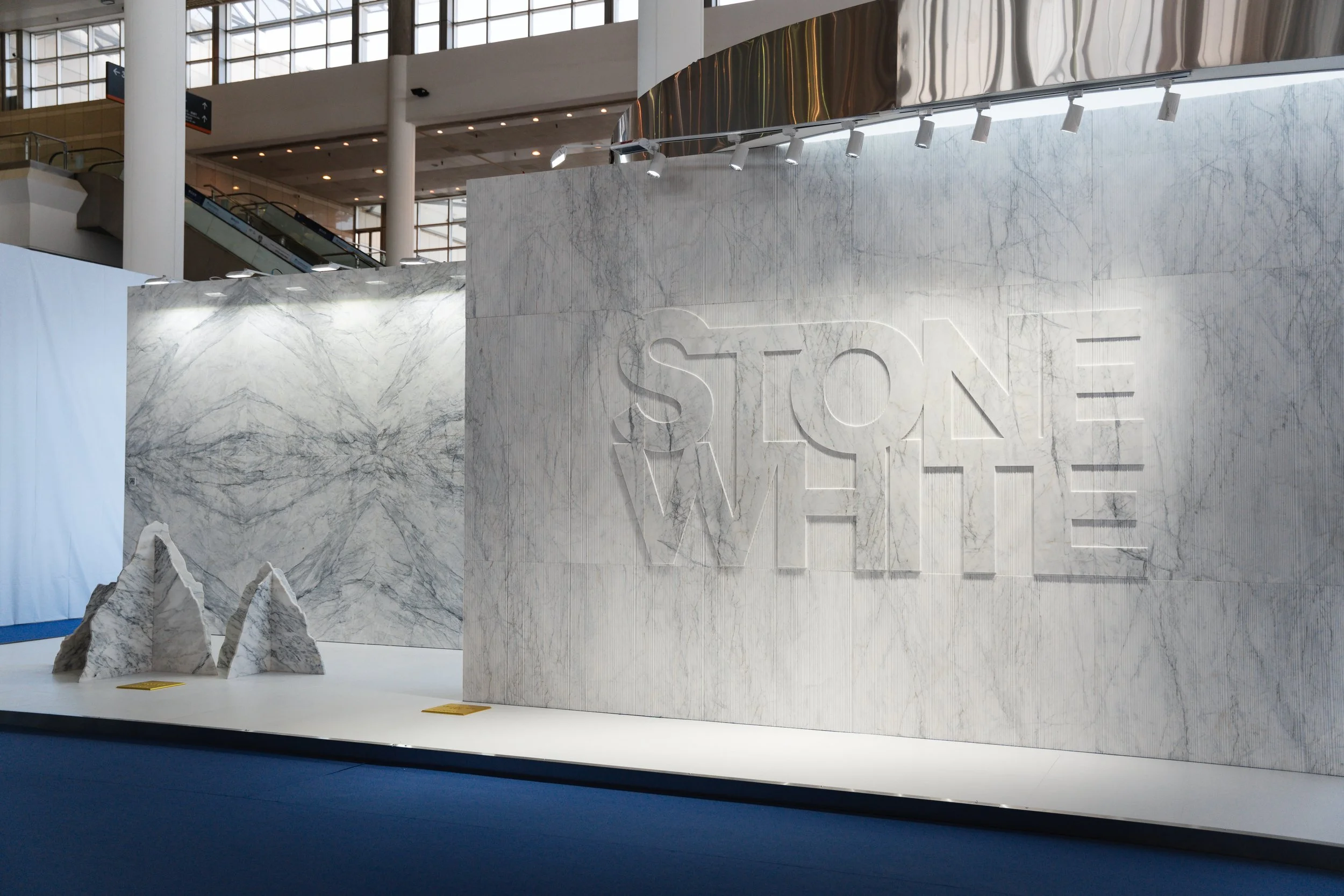 Exhibit with large white marble panels, some with gray veining, and the words 'STONE WHITE' engraved on one panel, displayed in a spacious, modern indoor setting.