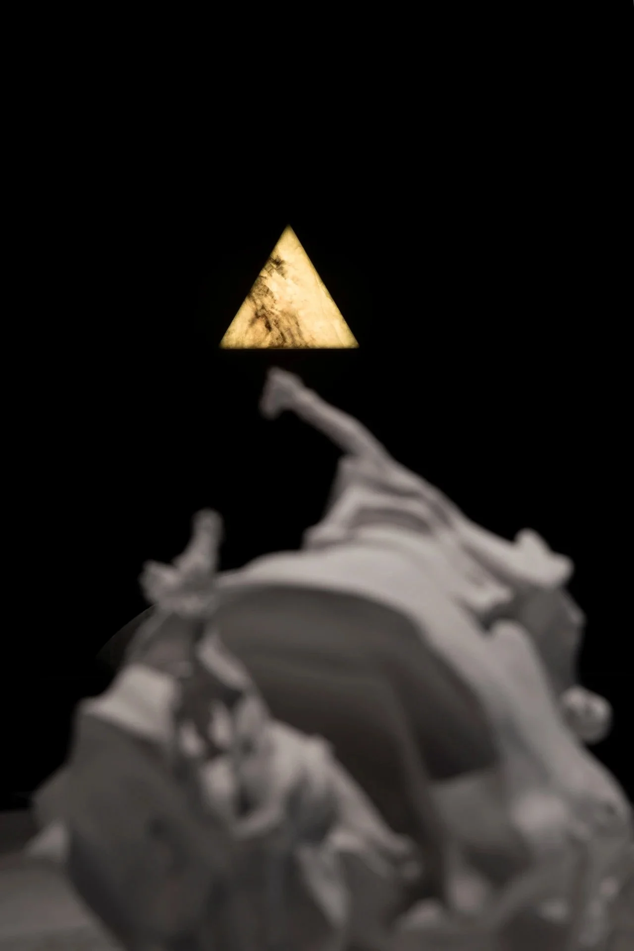 Close-up of a sculpture resembling a wolf with a triangle-shaped light above it, against a black background.