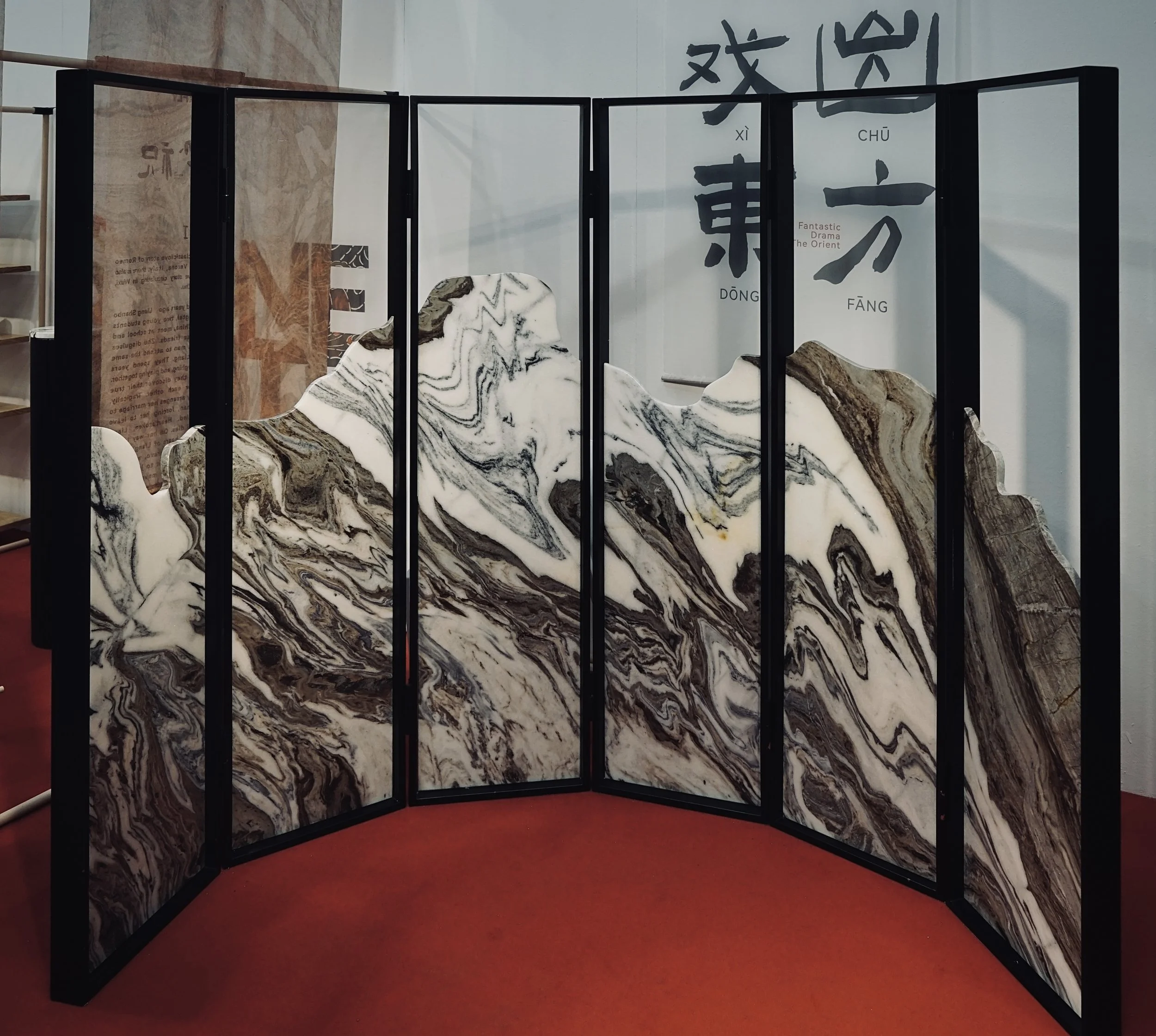 A black folding screen with marble-patterned panels, set on a red carpet at an exhibition or gallery, with Chinese characters and text in the background.