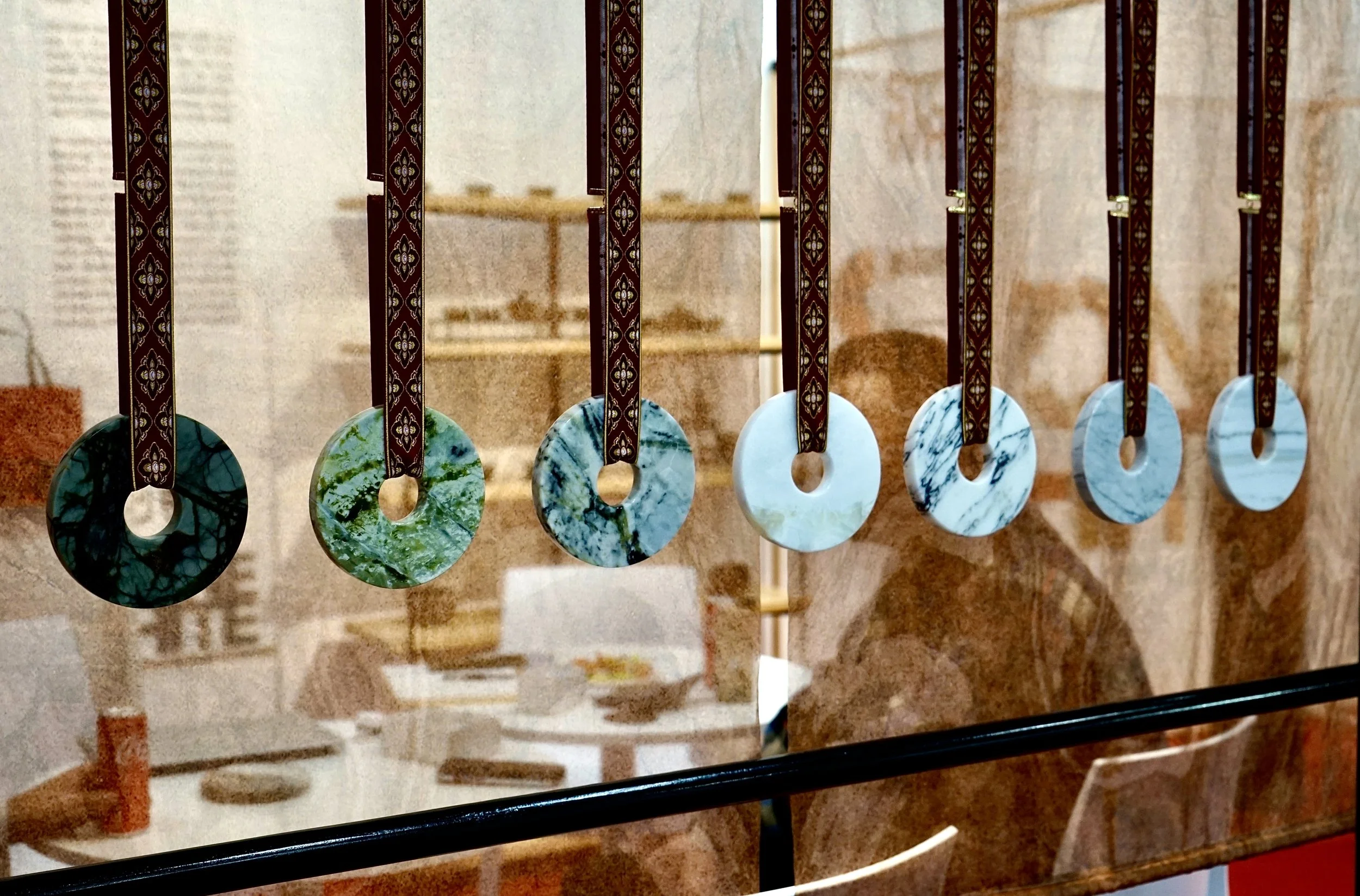 Collection of six circular jade pendants hanging from decorative ribbons behind a glass window.
