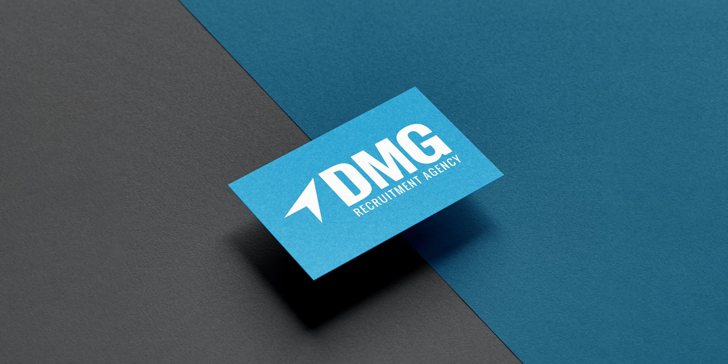 Blue business card with white text reading 'DMG Recruitment Agency' and a stylized arrow logo, placed on a split black and blue background.