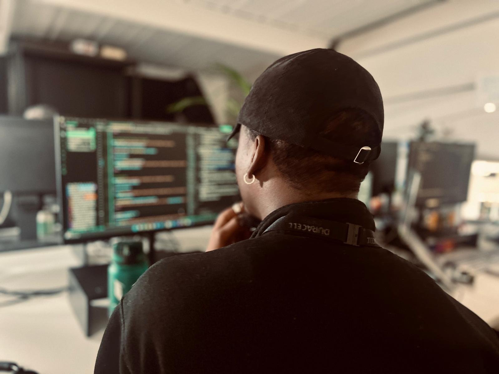 Person working on multiple computer screens in an Puredrive Energy/Duracell Energy, wearing a black cap