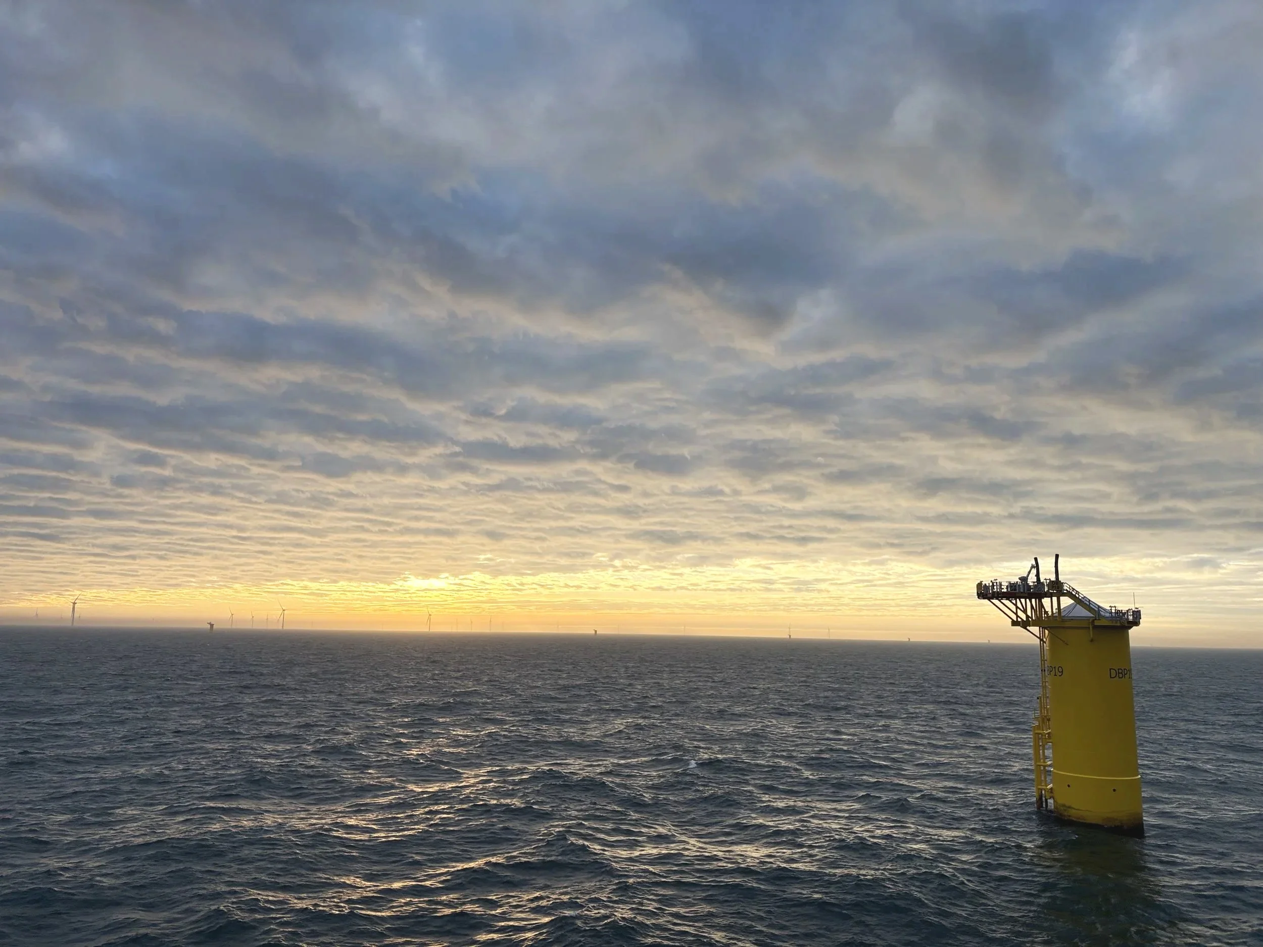A body of water under a cloudy sky at sunset with a yellow offshore oil platform structure in the water.