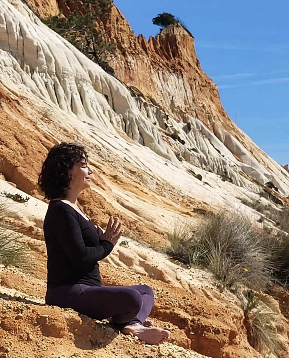 A woman practicing meditation outdoors on a sandy slope with desert rock formations in the background.