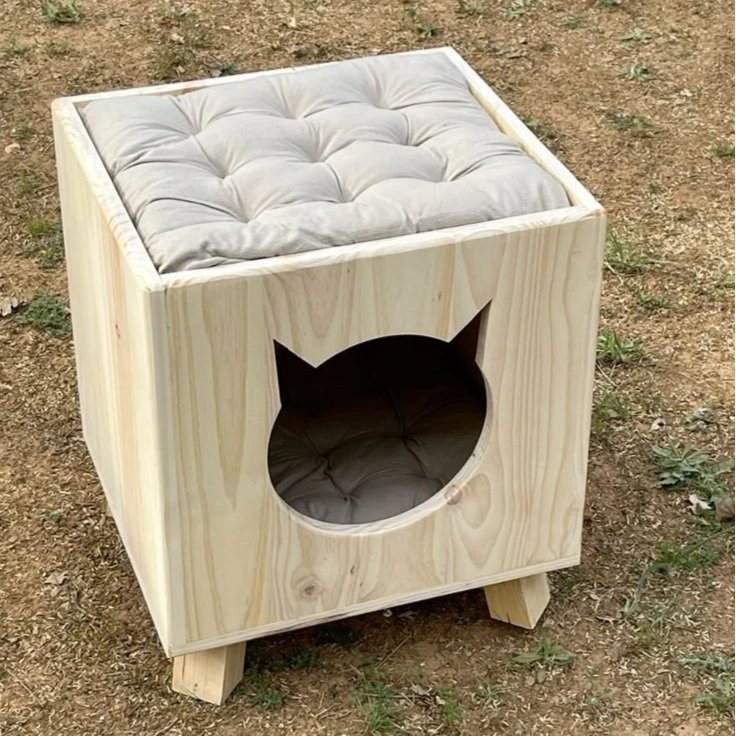 Hundehaus aus Holz mit Katze-Silhouette an der Vorderseite, mit einem weichen weissen Kissen auf der Oberseite, draußen auf dem Boden stehend. Handwerker Workshop für Frauen