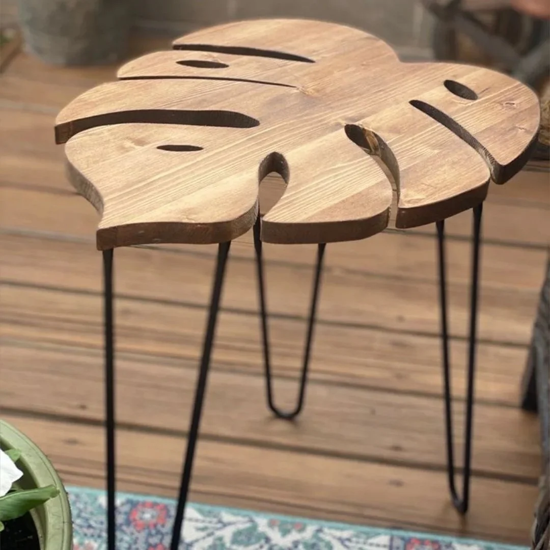 Holztisch in Form eines Monstera-Blattes mit schwarzen Metallbeinen.