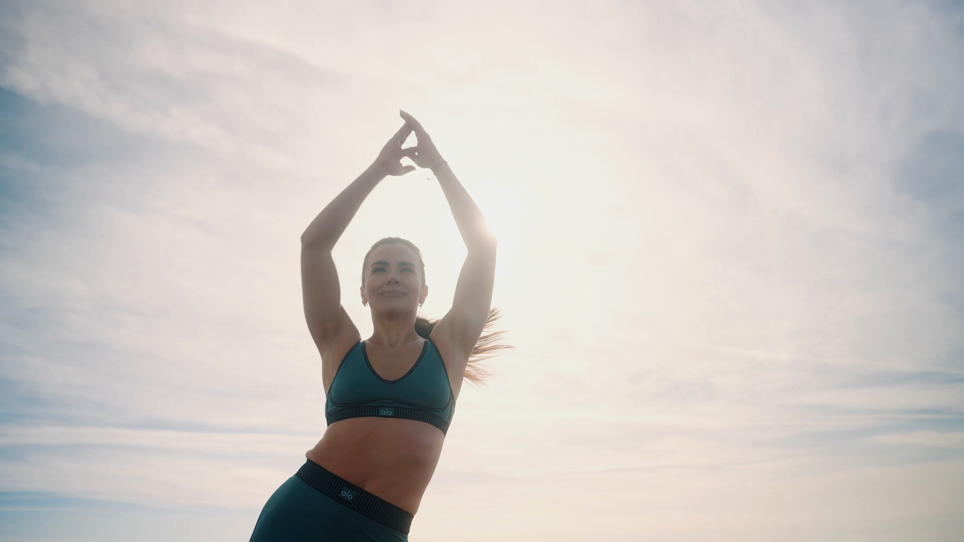 A woman in athletic wear performs a yoga pose outdoors during sunrise or sunset.