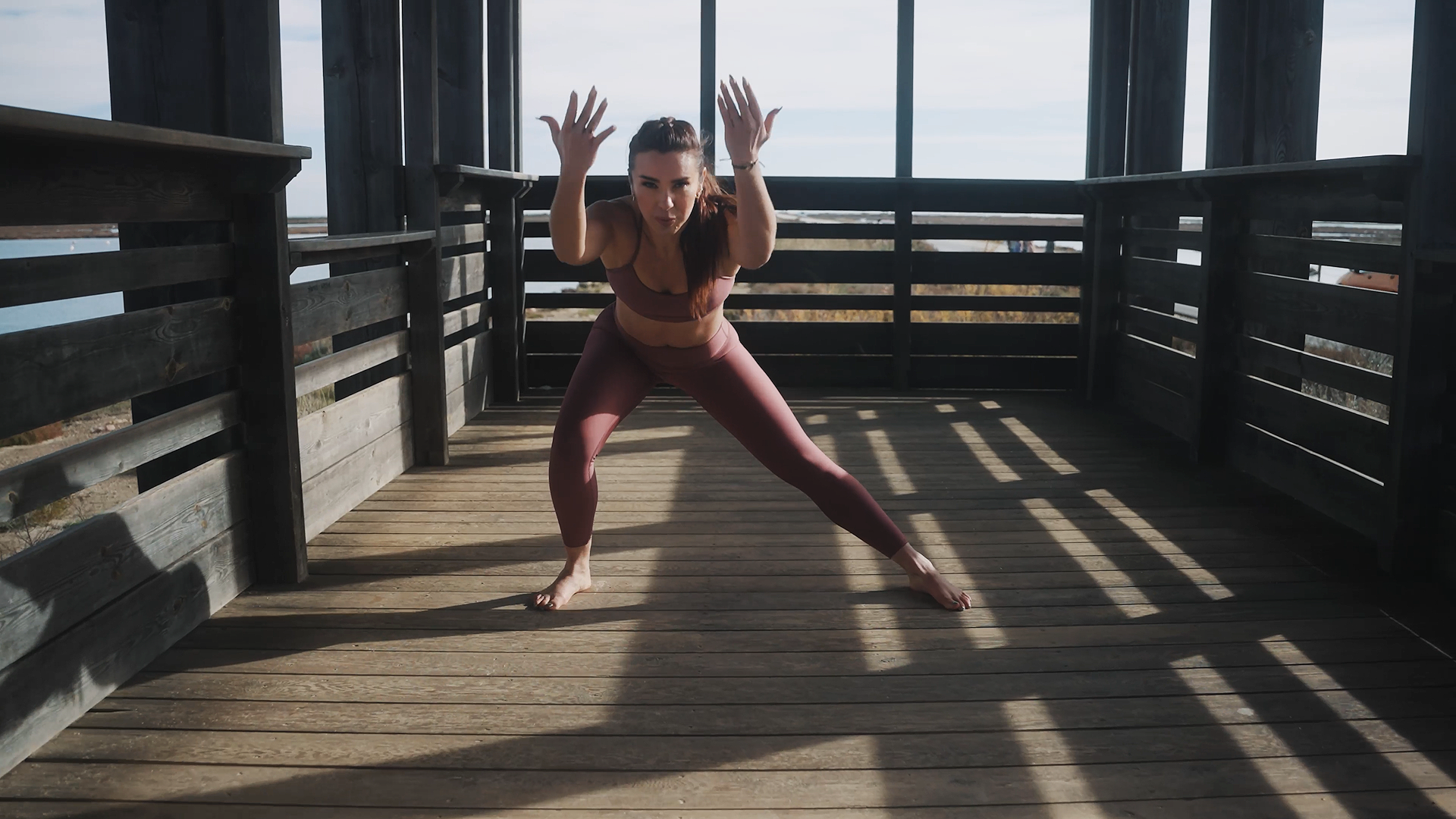 Woman in activewear doing a yoga pose on a wooden deck outdoors.