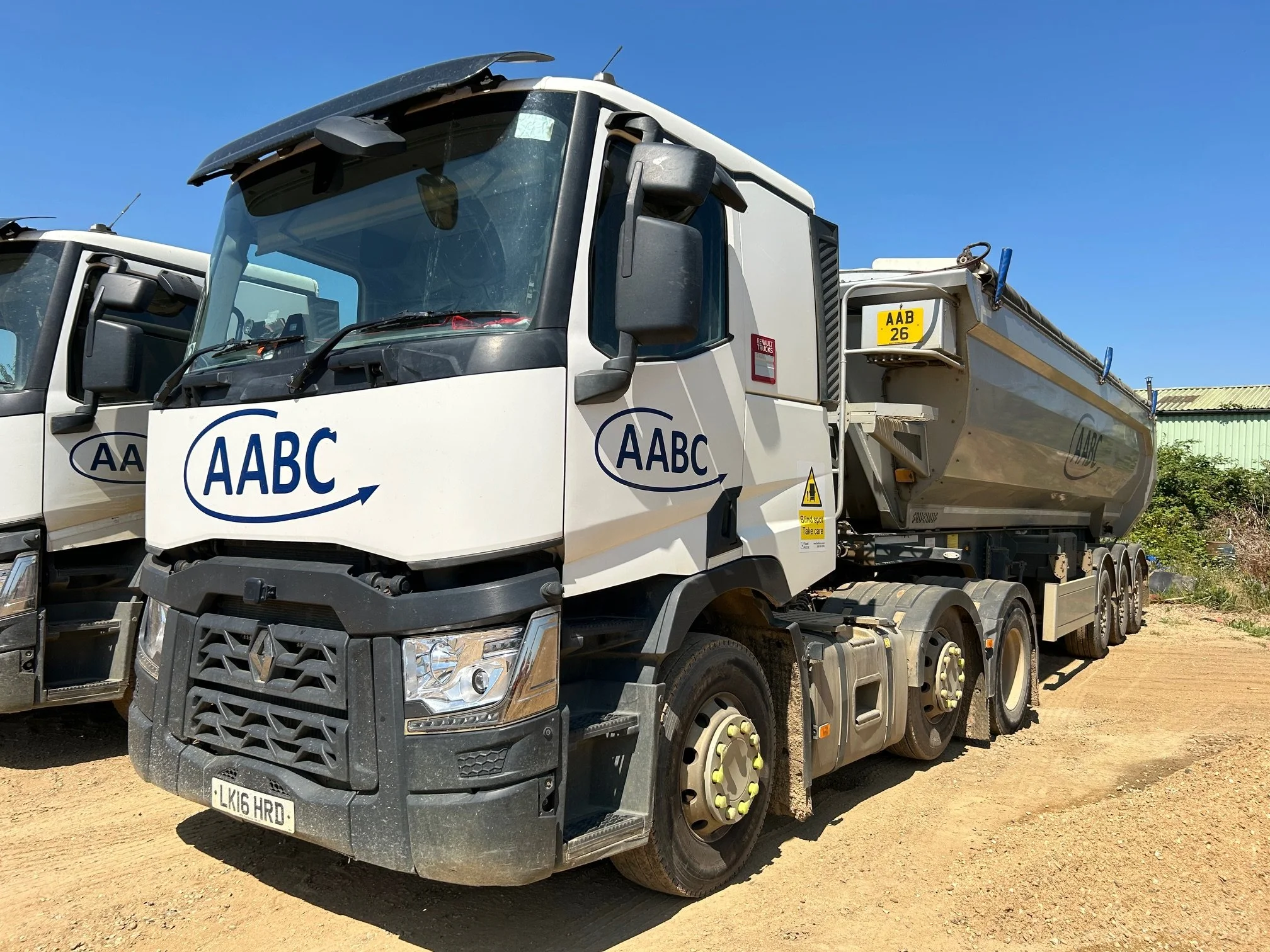 A white tanker truck with AABC company logo parked on a dirt lot under a clear blue sky.