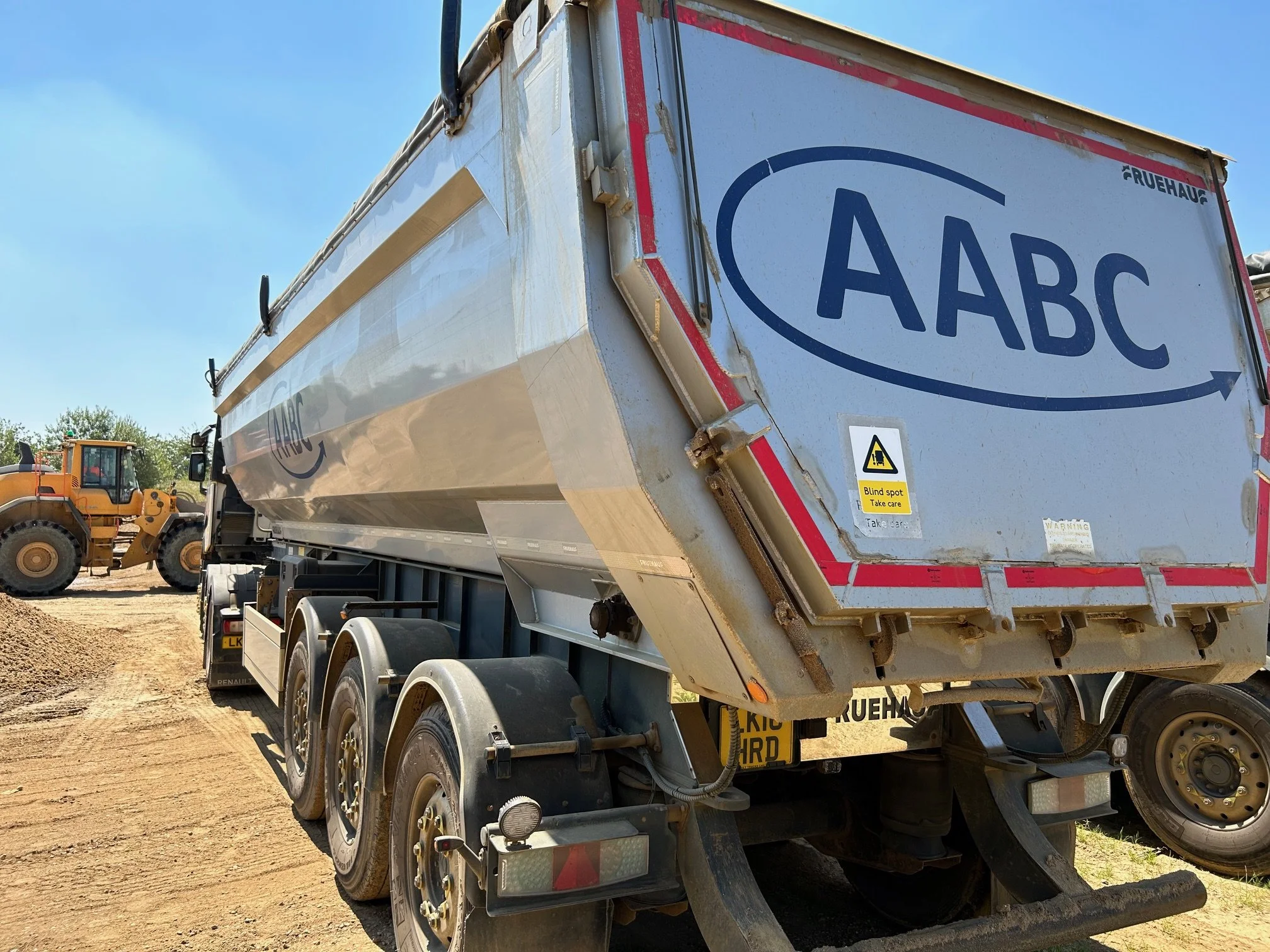 A large AABC trailer or container on a construction or industrial site, with a blue sky and a bulldozer in the background.