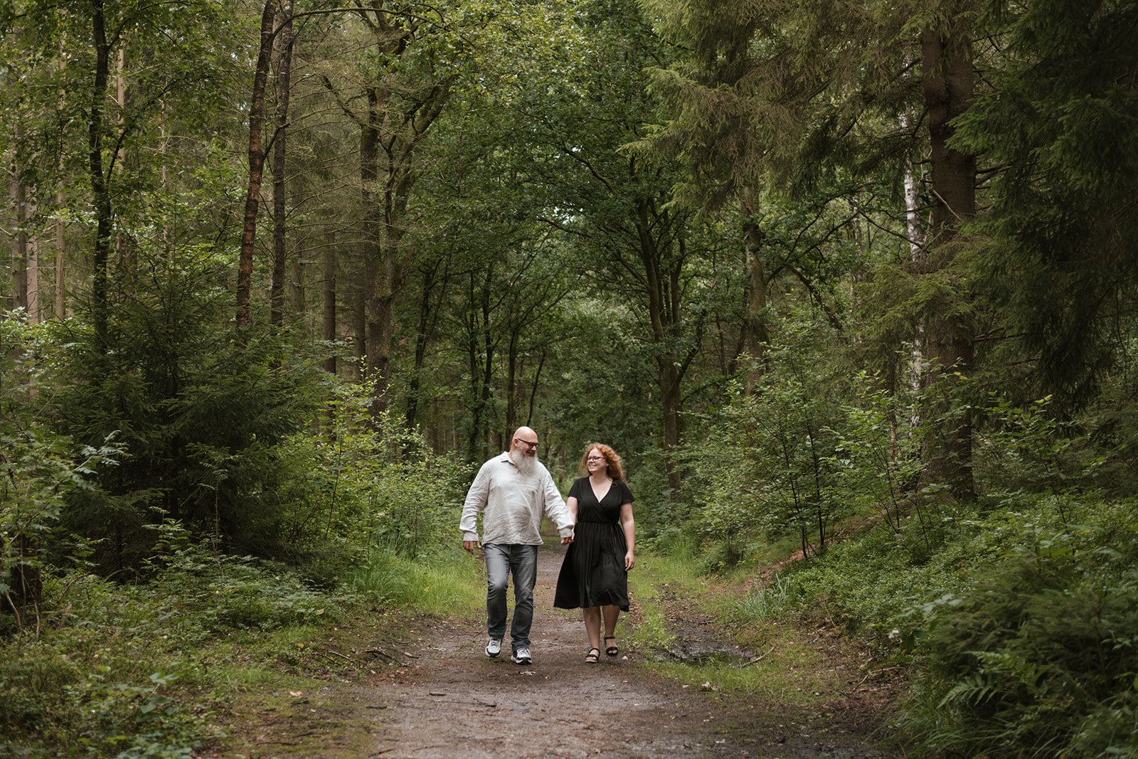 Ein Mann und eine Frau gehen Hand in Hand den Waldweg entlang.