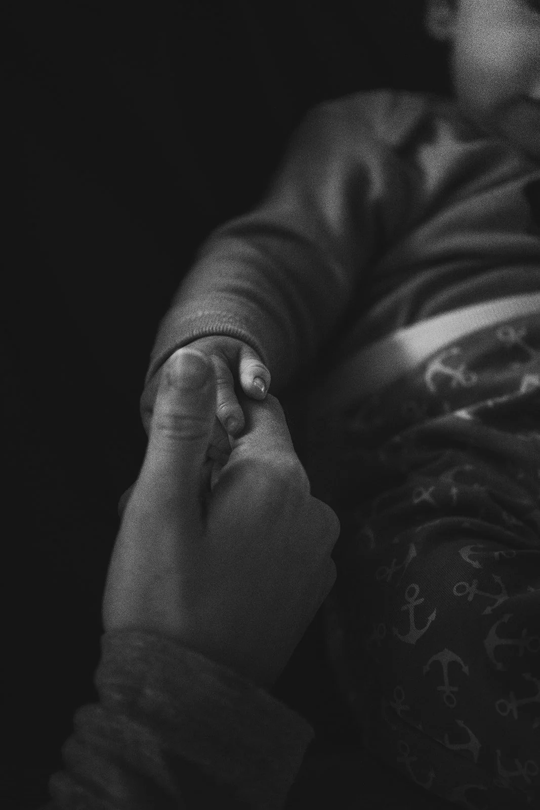 Nahaufnahme eines kleinen Kindes, das eine erwachsene Hand hält, in Schwarz-Weiß.
