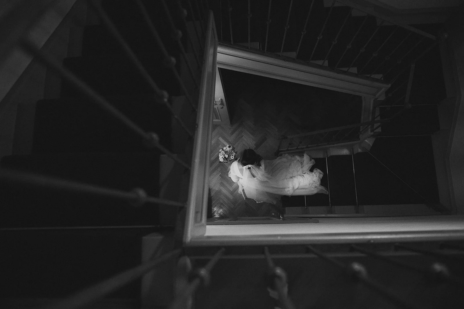 Eine Frau in einem Hochzeitskleid steht auf einer Treppe und schaut nach unten, betrachtet eine Blumenstrauß.