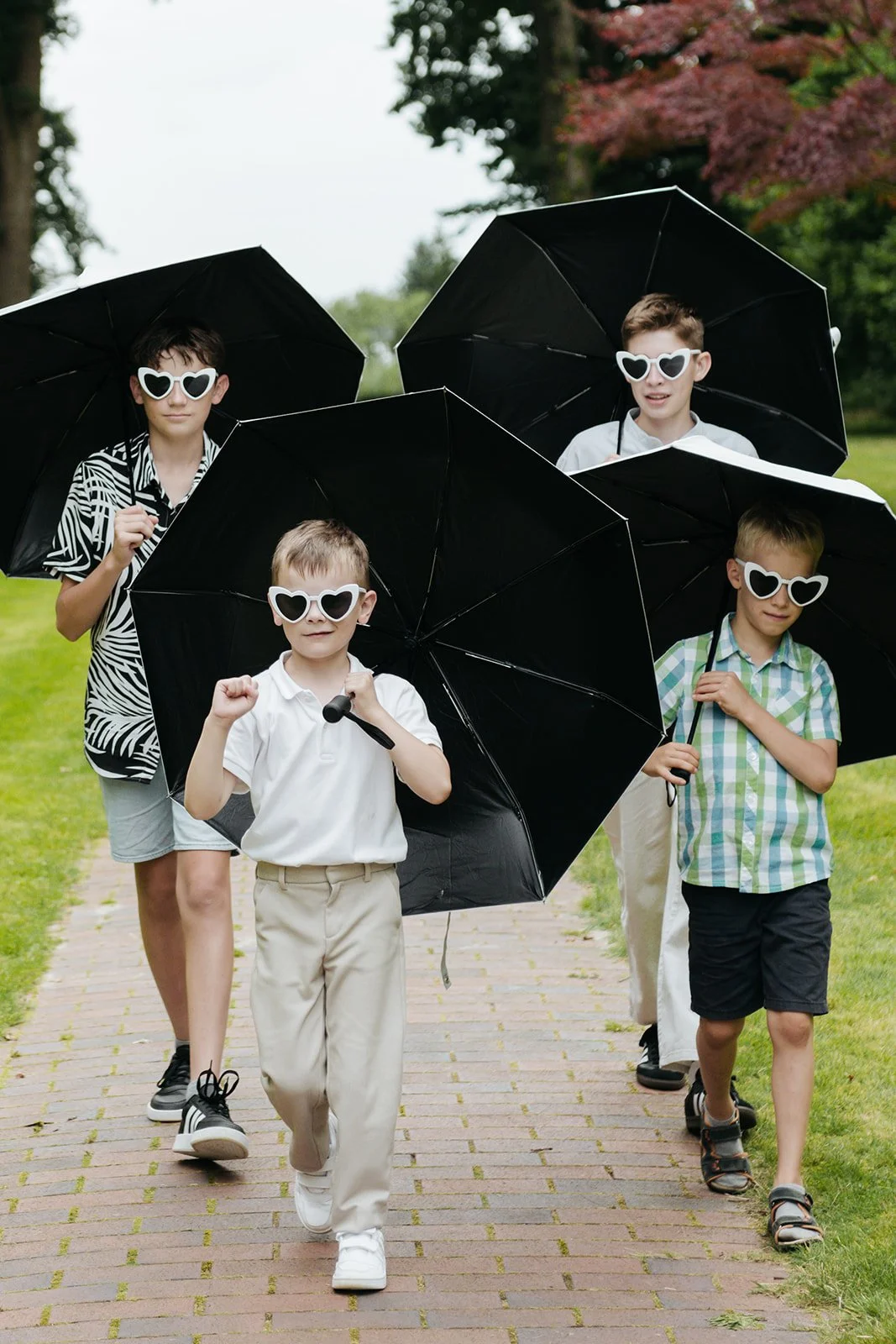 Kinder bei der Hochzeit im Park tragen Sonnenbrille und Spielen mit Regenschirme.