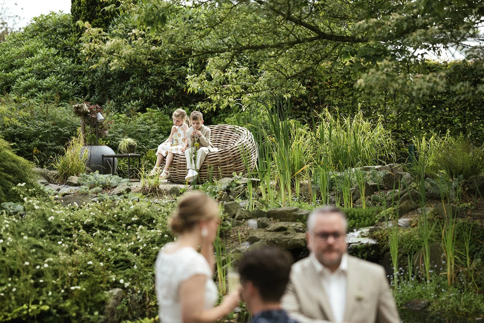 Kinder sitzen auf einem Gartenmöbel im Park nach der standesamtliche Trauung.