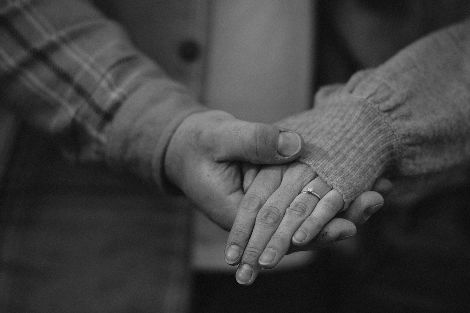 Ein Mann hält eine Hand einer Frau, die einen Ring trägt, in einer Geste der Unterstützung oder Liebe.