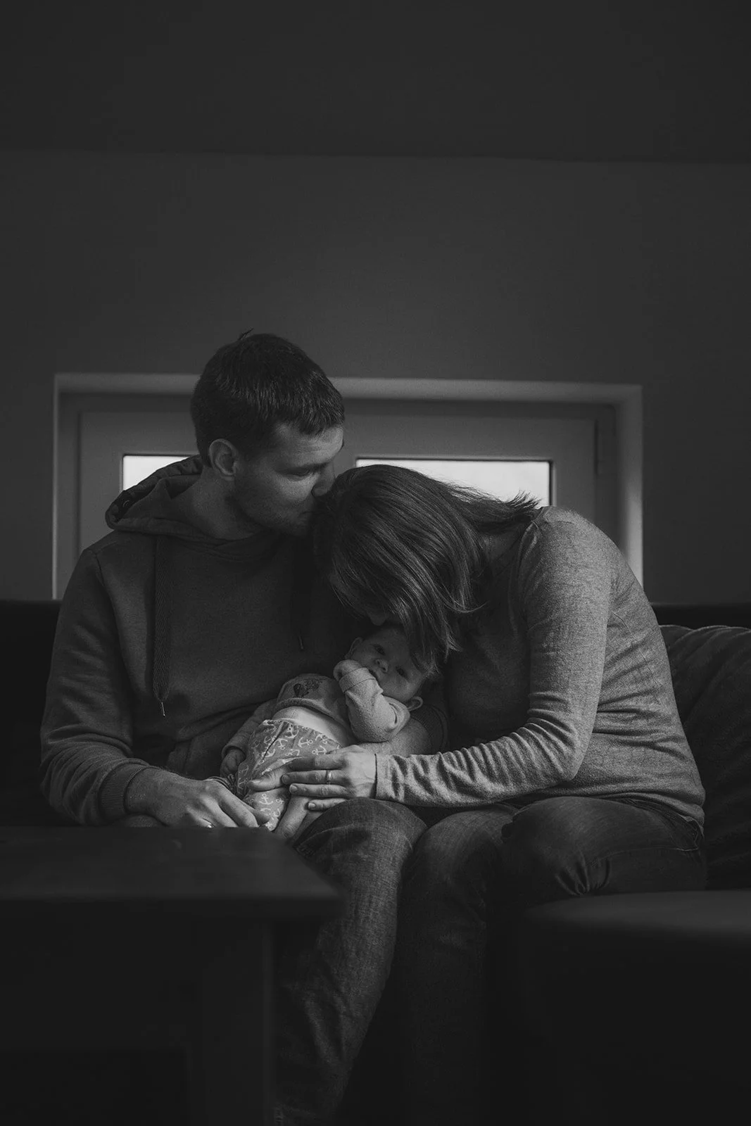 Familie mit kleinem Kind, die sich auf der Couch kuschelt, im Schwarz-Weiß-Foto. Homestory in Ostfriesland