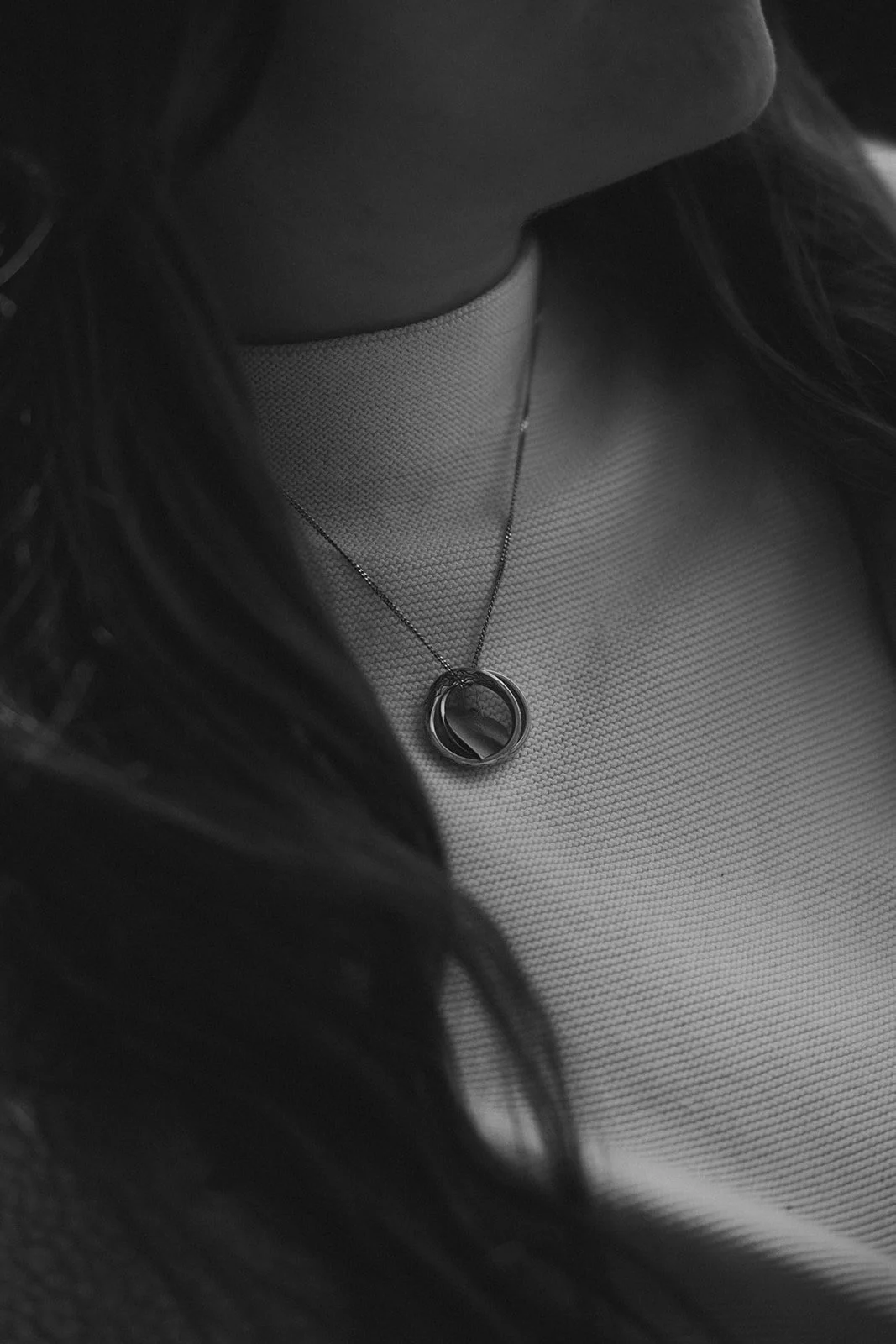 Nahaufnahme eines Halsbands mit einem Anhänger an einer Person, schwarz-weiß, mit langem dunklem Haar.