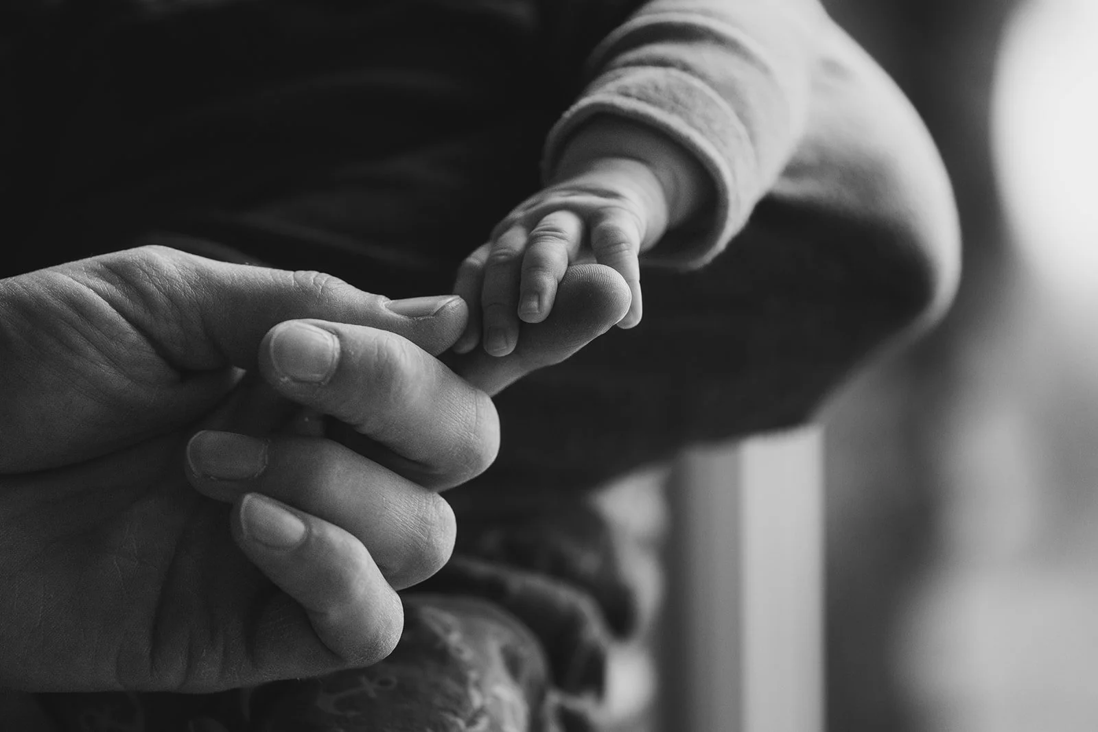 Ein Erwachsener hält die kleine Hand eines neugeborenes Babies. Die Szene ist in Schwarz-Weiß. Das Bild symbolisiert Fürsorge und Verbindung.