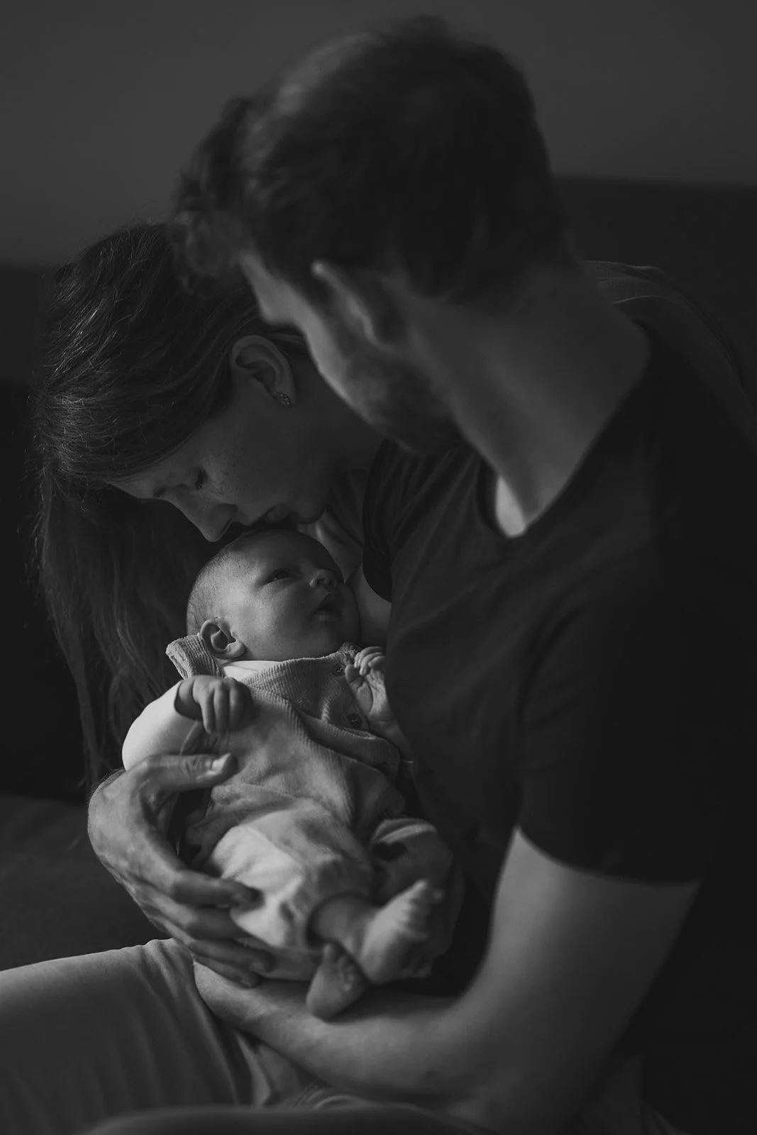 Vater hält sein neugeborenes Baby in der Hand. Mutter küsst das Baby am Kopf.