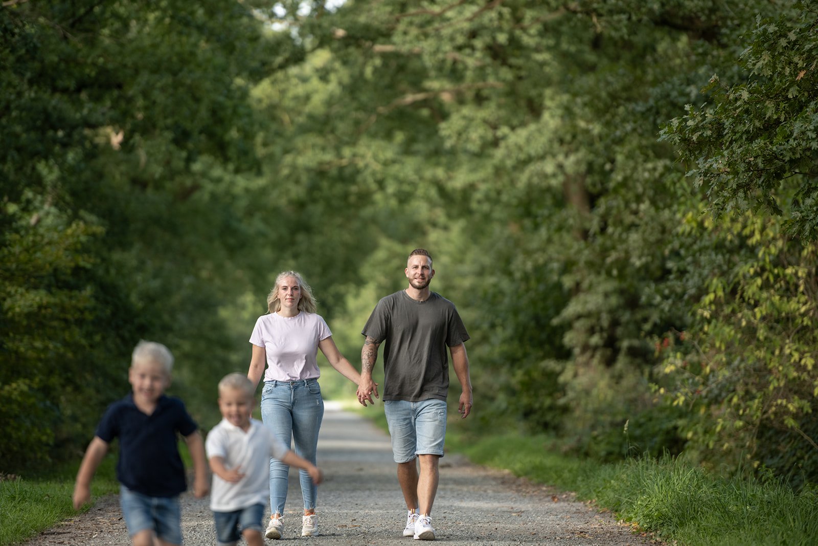 Familie macht einen Spaziergang in der Natur auf einem geraden Weg, umgeben von Bäumen und Grünflächen.