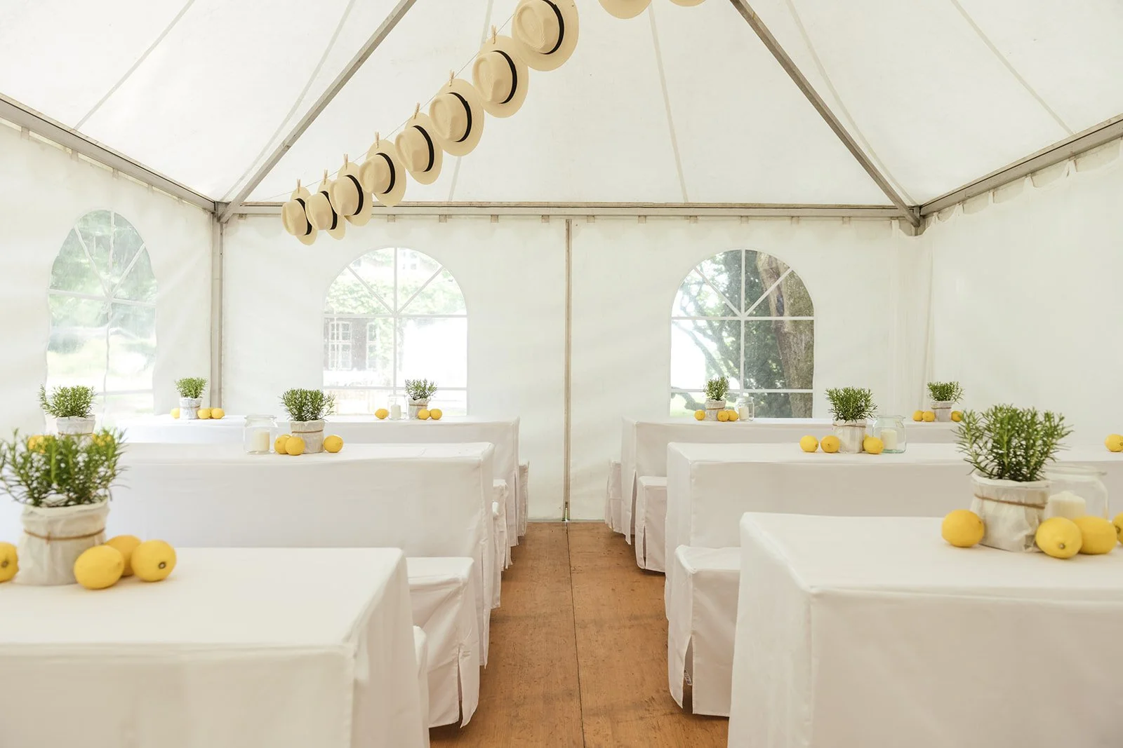 Hochzeitszelt mit Tische und Tischdecken, dekoriert it Rosmarin und Zitrone. Helles Licht tritt durch das Zeltfenster. 