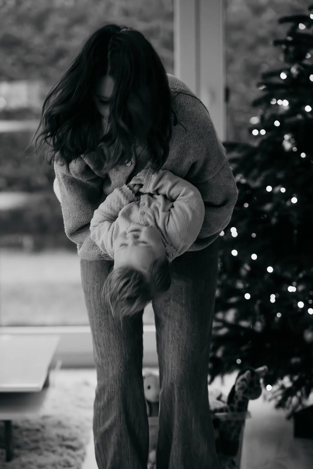 Eine Frau hält ein lachendes Kind im Saunakleid, während sie vor einem Weihnachtsbaum steht.