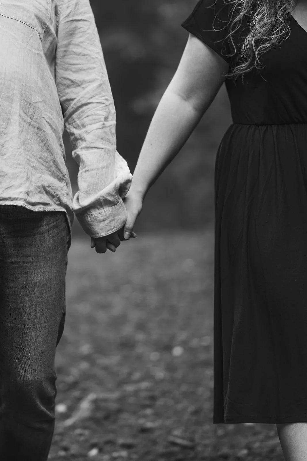 Ein Mann und eine Frau halten sich an den Händen, die Nahaufnahme zeigt nur ihre Hände und Beine, in Schwarz-Weiß aufgenommen.