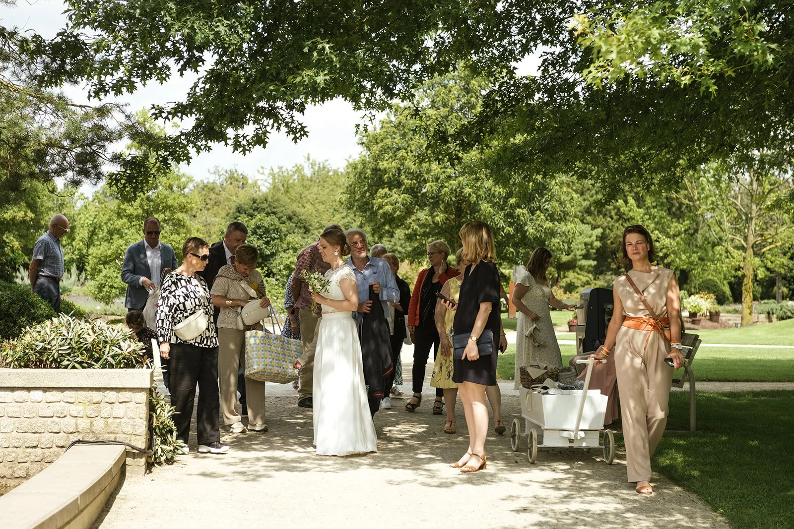 Hochzeitsgesellschaft wartet im Park. In der Mitte steht die Braut.