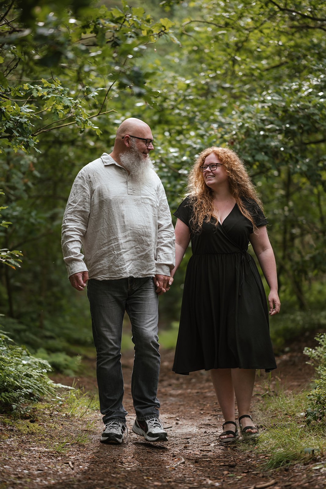 Ein Mann und eine Frau, die Händchen haltend durch einen Wald spazieren.