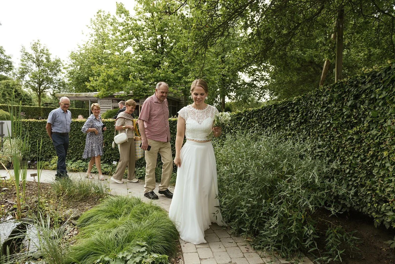 Braut mit Hochzeitsgesellschaft läuft im Park neben einem Teich.