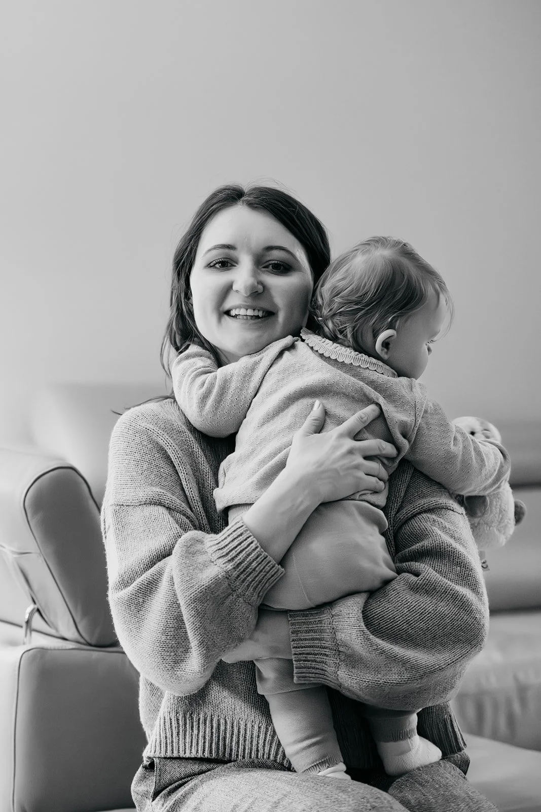 Eine lachende Frau hält ein Baby im Arm, während sie auf einer Couch sitzt.