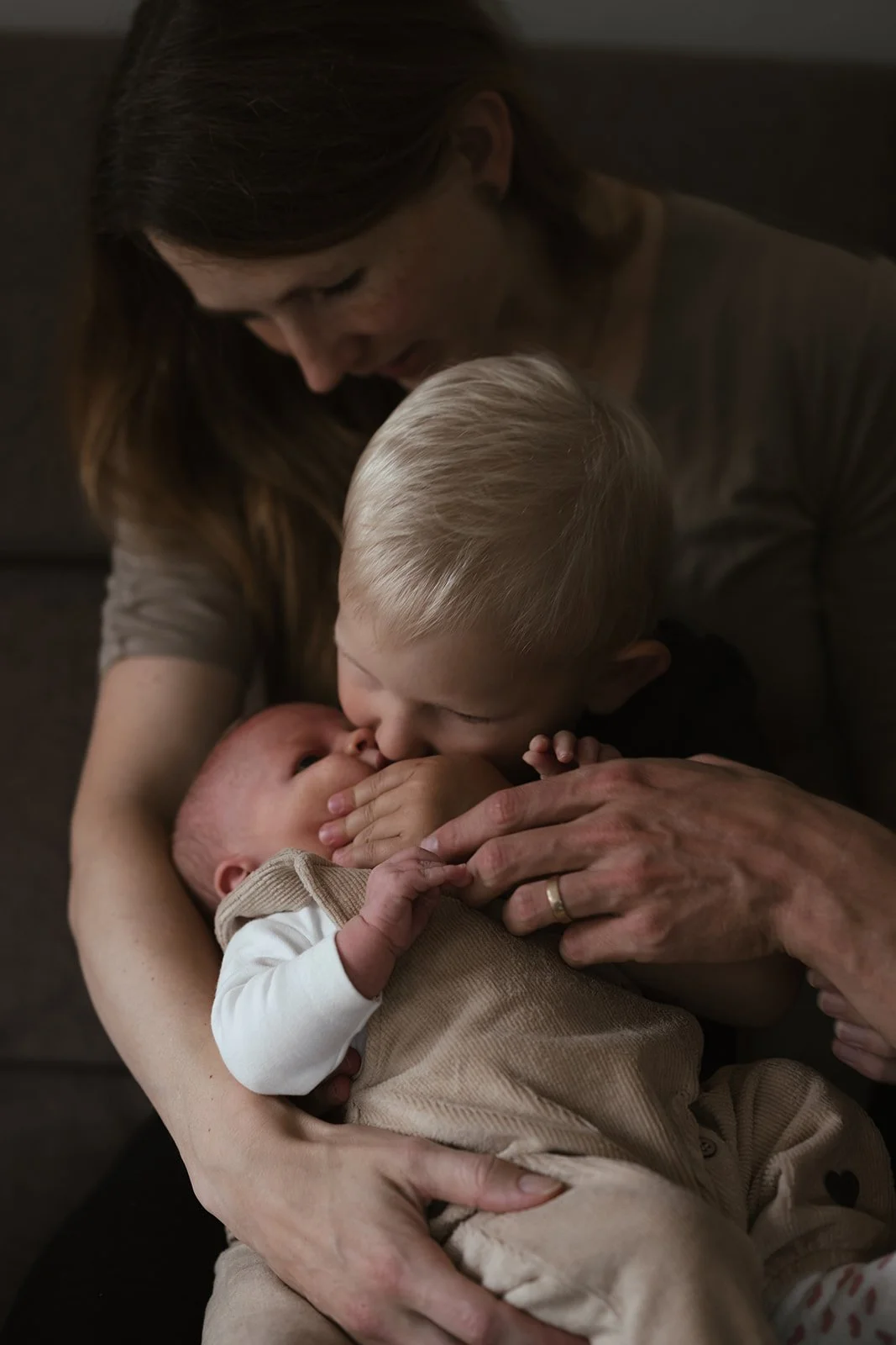 Eine Frau hält ein Baby im Arm, während ein älteres Kind das Baby küsst.