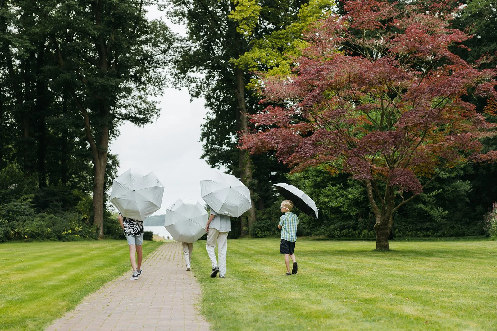 Kinder spielen mit Regenschirmen im Park während der Gartenparty nach der Trauung.