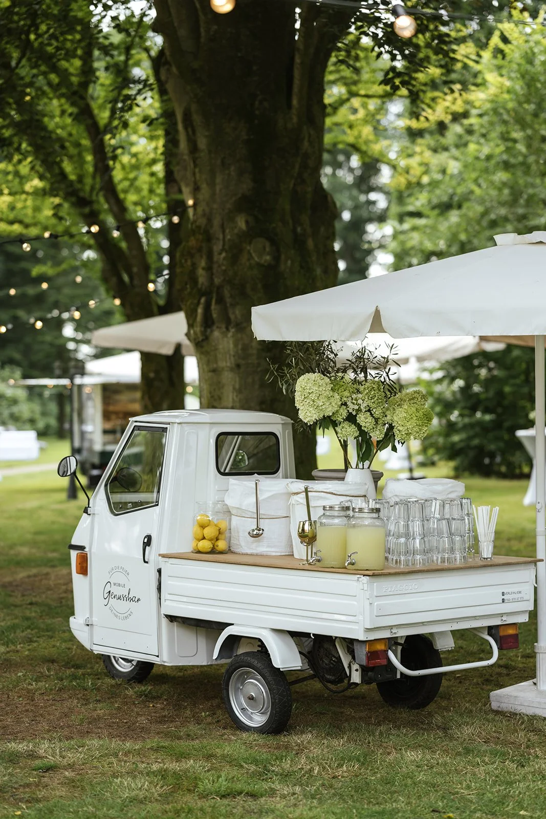 Ape von Piaggio steht im Park und wird als Genussbar benutzt, Getränke und Gläser stehen hinten drauf.
