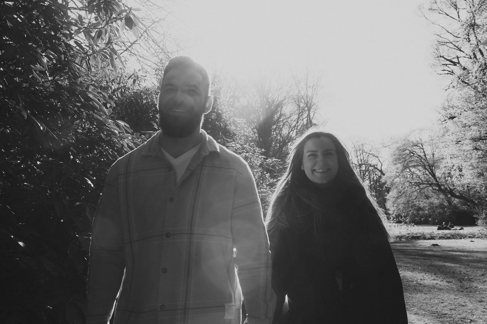 Paar schaut in die Kamera im Park. Verlobung mit Gegenlicht.