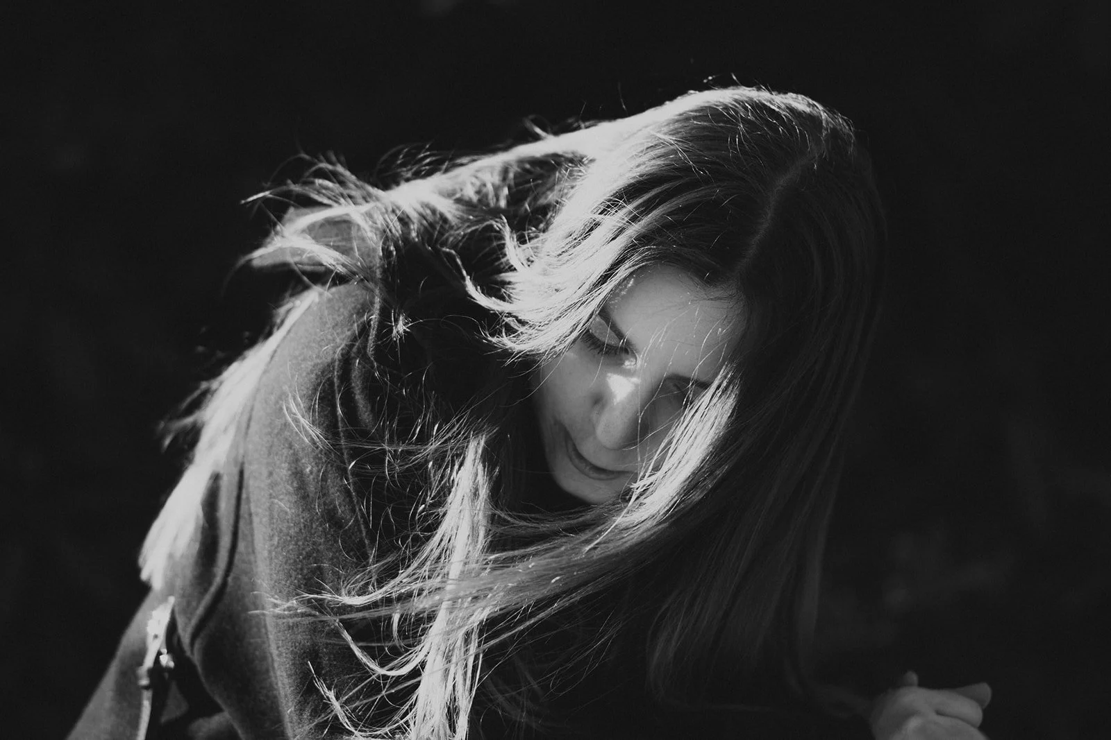 Schwarz-weiß-Fotografie einer lachenden jungen Frau mit langen Haaren, die in die Kamera schaut.