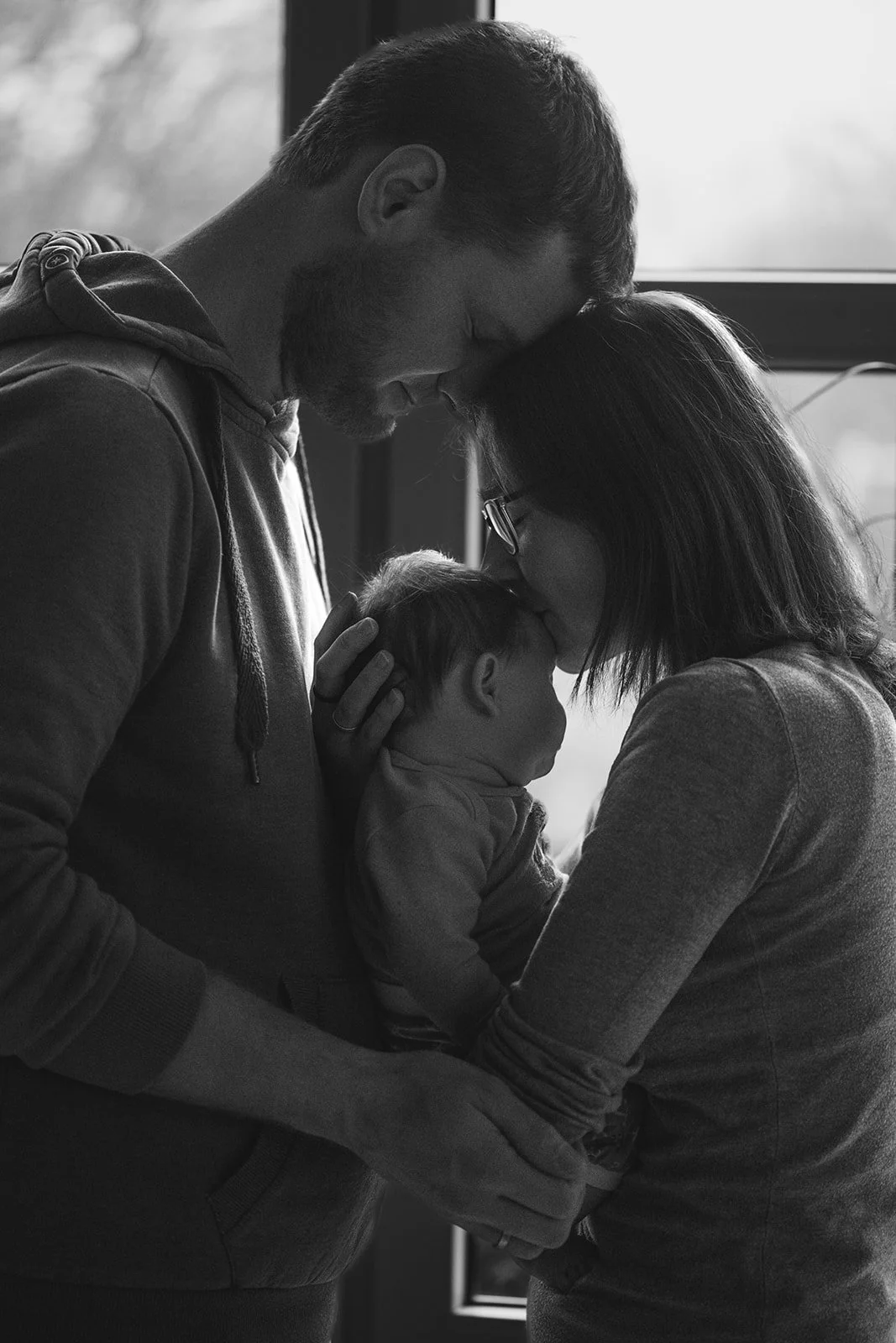 Ein Familienbild in Schwarz-Weiß: Ein Mann und eine Frau halten ein Baby, sie berühren ihre Stirn und zeigen Zuneigung und Liebe.