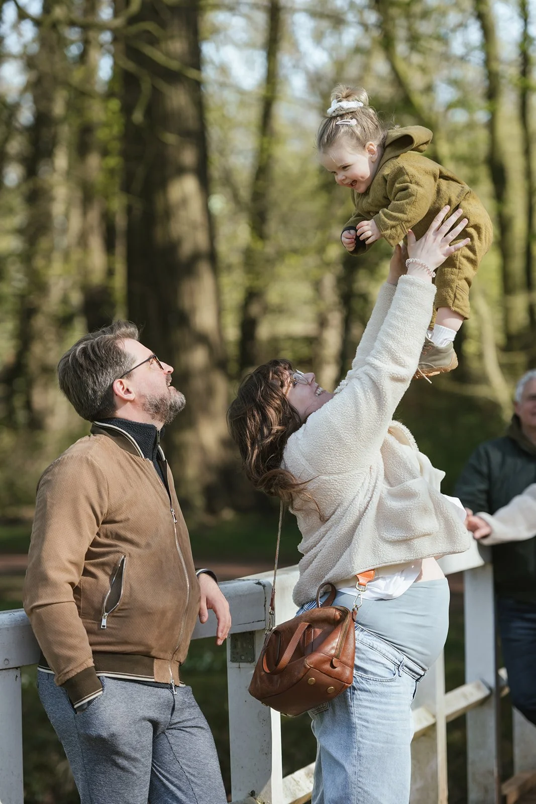 Familie im Grünen. Mutter hebt das Babay in die Luft, Vater lächelt sie an.