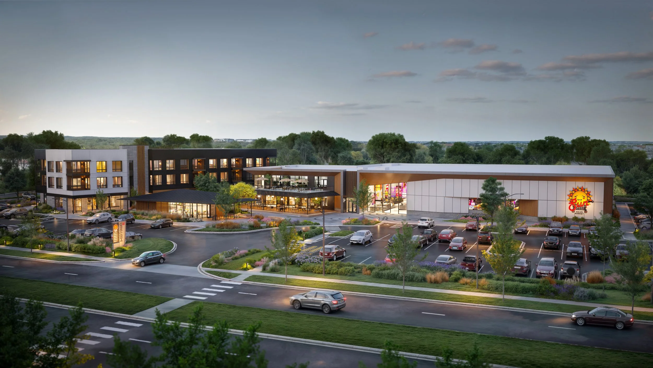 Modern shopping center with a large parking lot, surrounded by trees, with stores and cafes inside, including a Sun Asian Market, during evening hours.