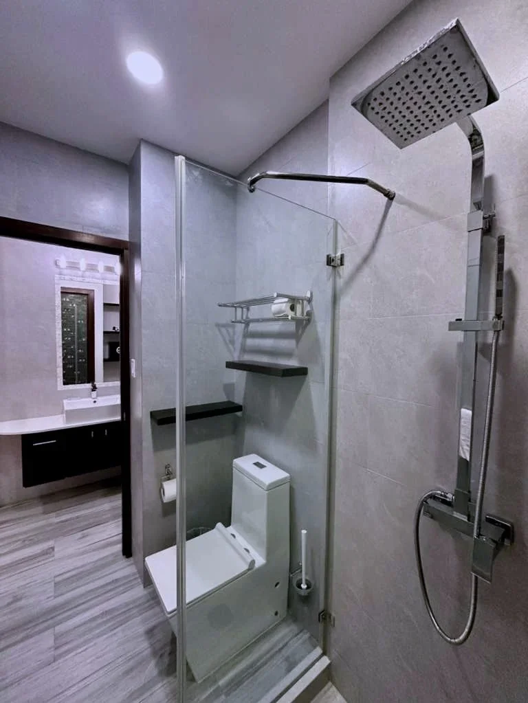 Bathroom with shower area, toilet, and separate sink area visible through a mirror. The bathroom has a modern design with grey tiles and wood-look flooring.  Unit S2, Caye Caulker,  Blu Zen Belize